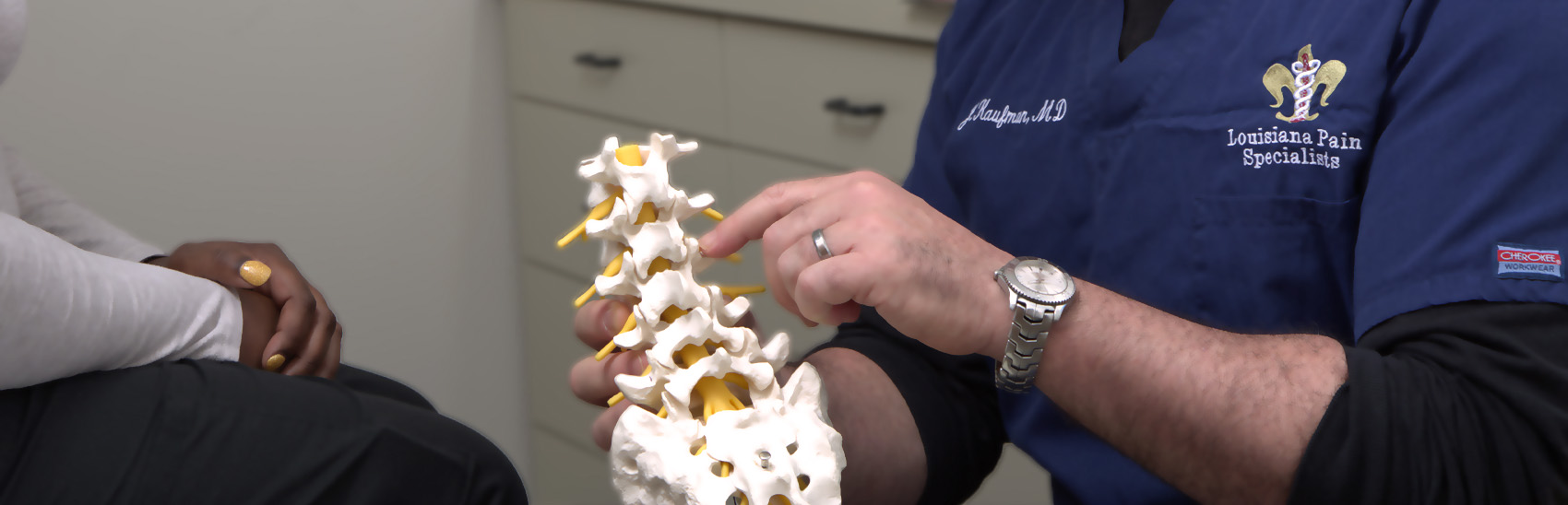 A Louisiana Pain Specialist doctor showing a anatomical model to a patient of a spine.